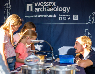 Children exploring artefacts and talking to an archaeologist in front of a Wessex Archaeology banner