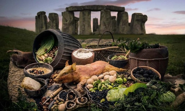 Selection of foods, many in prehistoric pottery vessels, in front of a Stonehenge